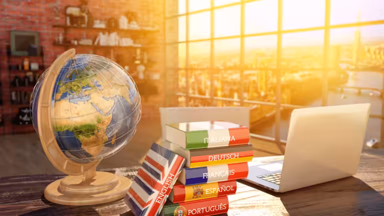 Lernen mit Leichtigkeit_Auf einem Tisch steht links ein Globus. Rechts daneben lieben mehrere Wörterbücher und daneben steht ein aufgeklappter Laptop.