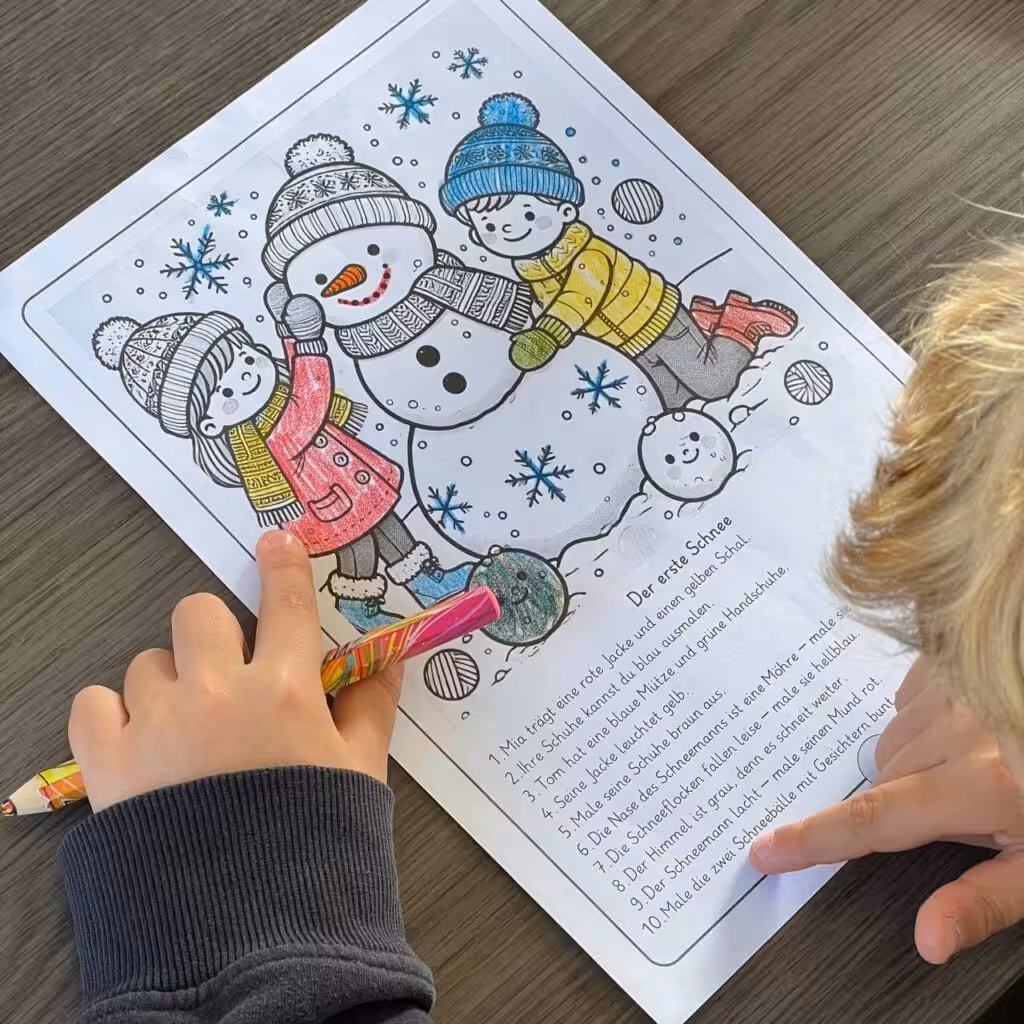 Ein Junge sitzt am Tisch und vor ohm liegt ein Arbeitsblatt mit einem Winterbild (2 Kinder bauen einen Schneeman). ES ist ein Ausmalbild mit 10 Sätzen. Das Kind zeigt mit seinem Finger auf einen Satz. Das Bild zum Ausmalen zeigt einen Elch im Garten. Es ist Winter. Unter dem Bild stehen 10 Sätze.